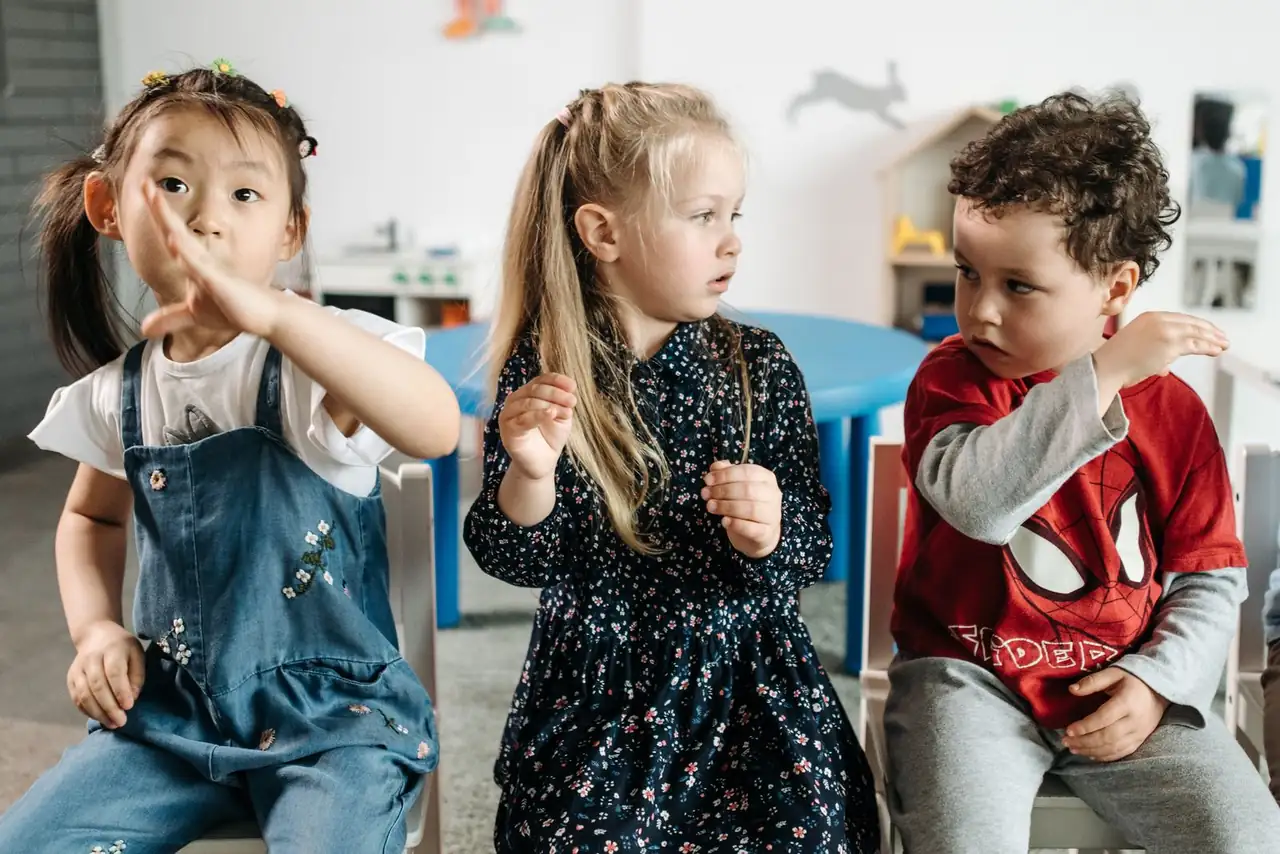 Three diverse children seated indoors, interacting in a playful classroom environment.
