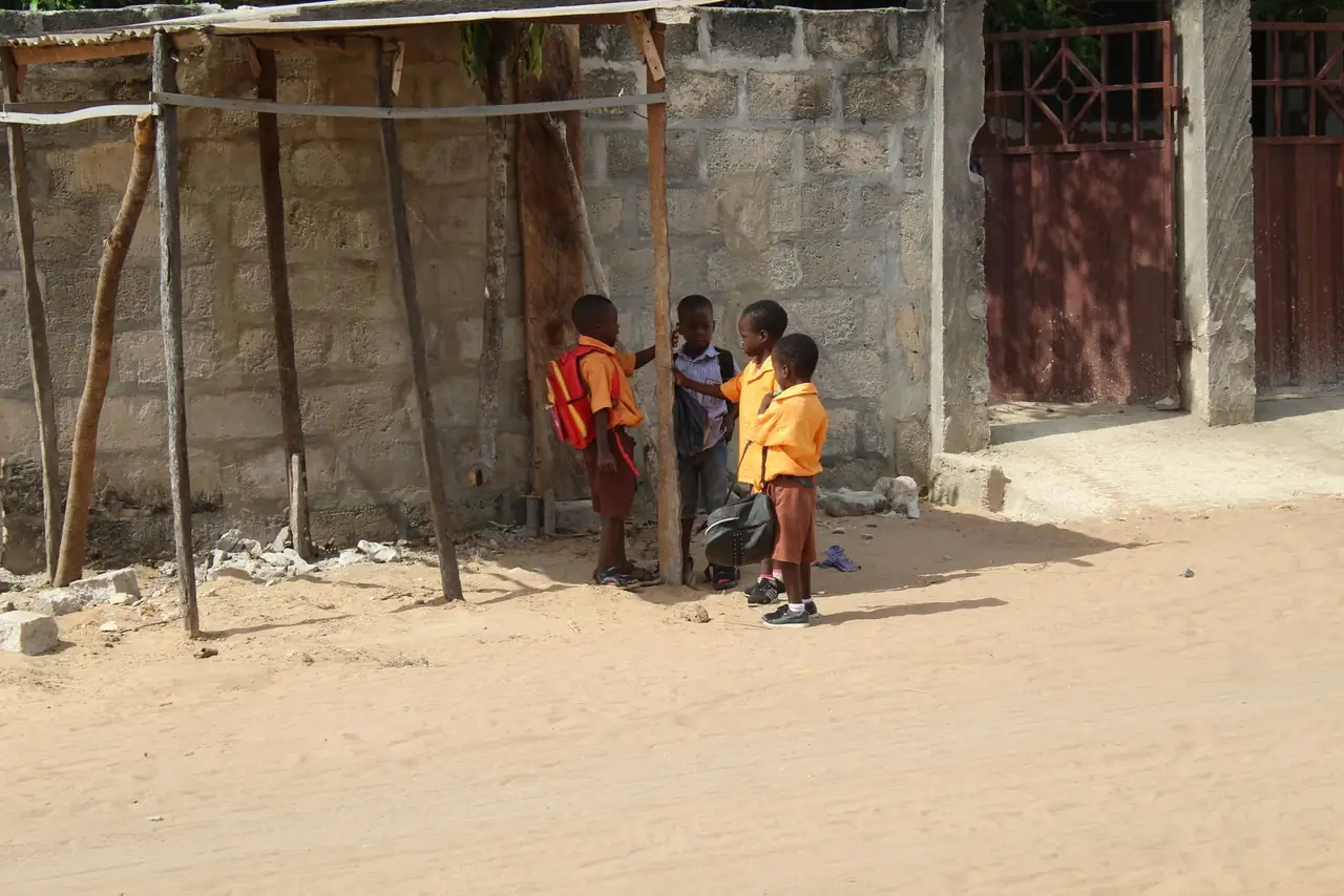 Group of children in school uniforms standing outside in a sunny Ghanaian neighborhood.